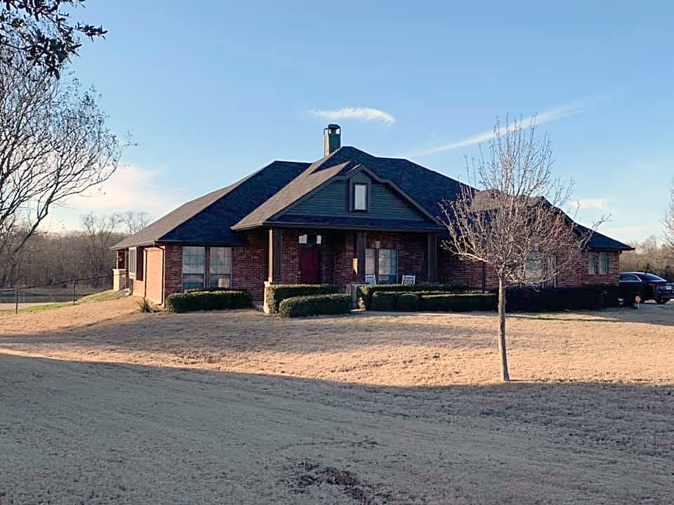 A brick home with a dark shingle roof on a wide country lot