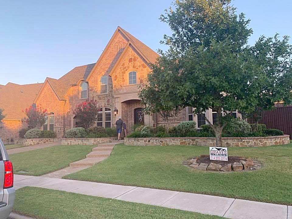 A large brick home with a steep shingle roof in evening light