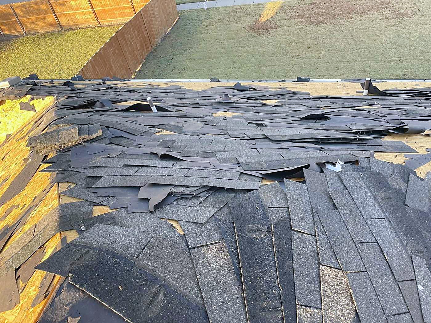 Old shingles stripped off and piled beside new underlayment during a tear-off