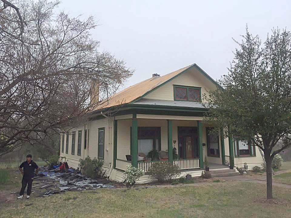 A bungalow with a new shingle roof and a crew member clearing old shingles from the yard